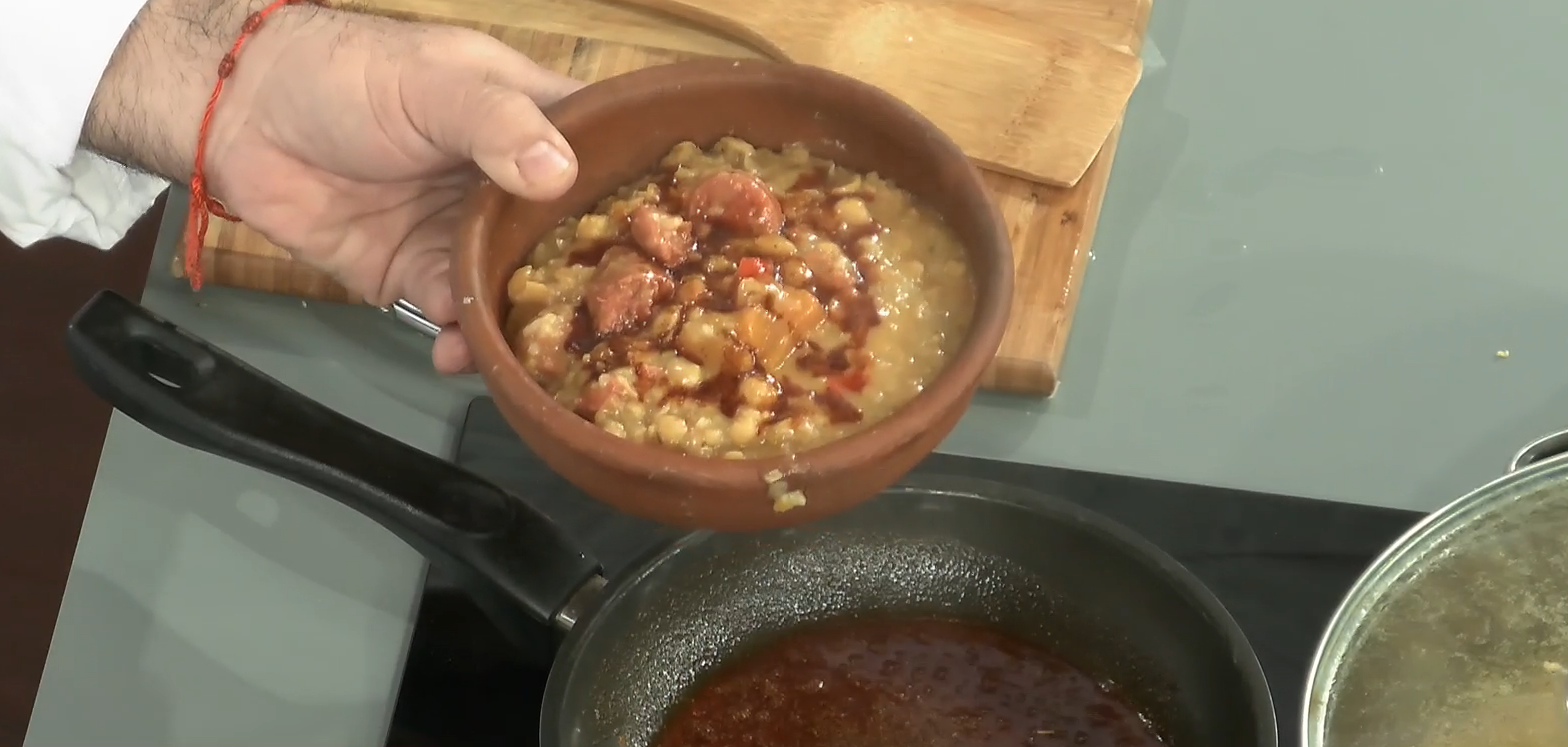 Una mano sosteniendo un plato de greda con garbanzos dentro