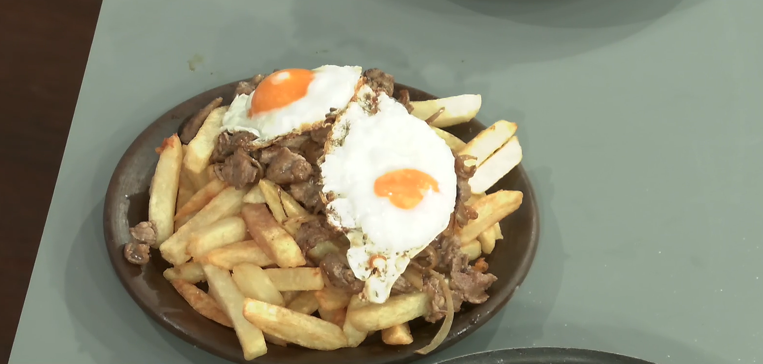 Un plato de greda con papas fritas, cebolla frita y dos huevos fritos.